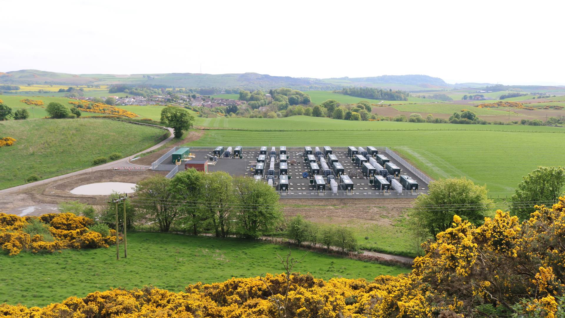 India BESS customs duty: rows of containerised grid-scale battery storage units at a utility battery storage site in a green valley